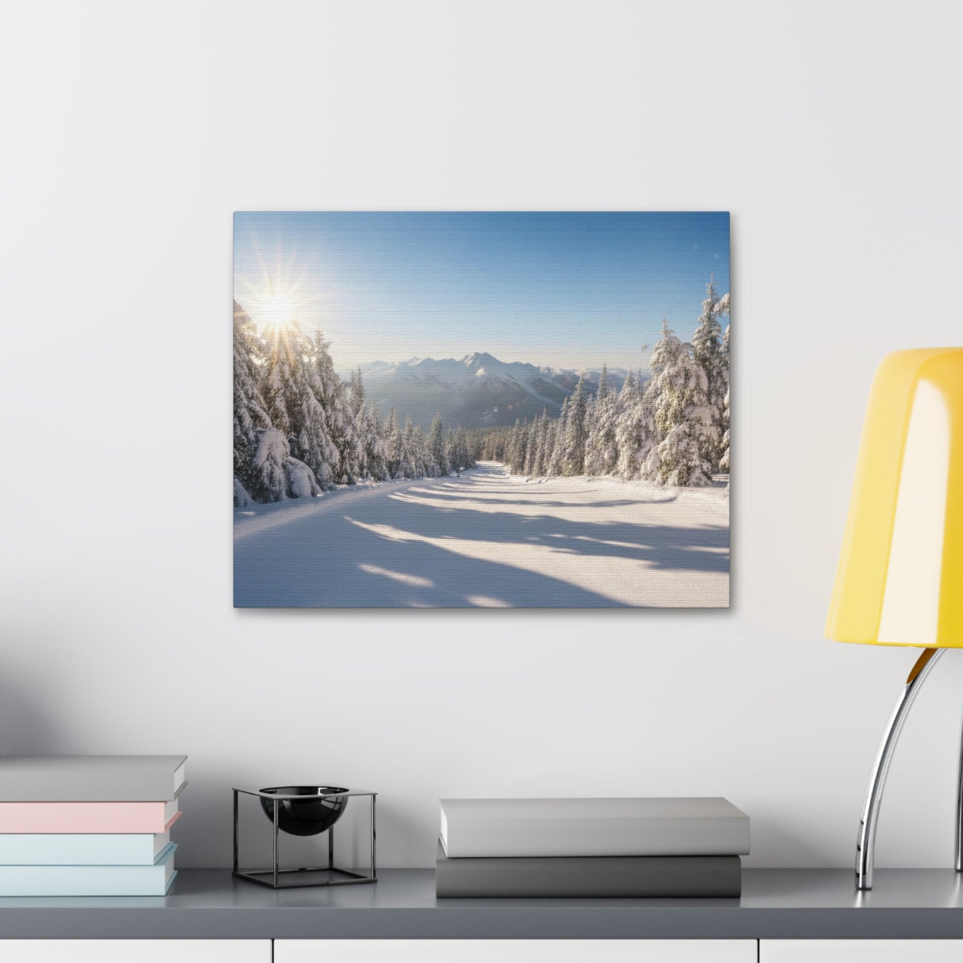 Canvas wall art of a serene wintry trail with snow-covered pines and mountains under a clear sky, framed and mounted on a white wall.