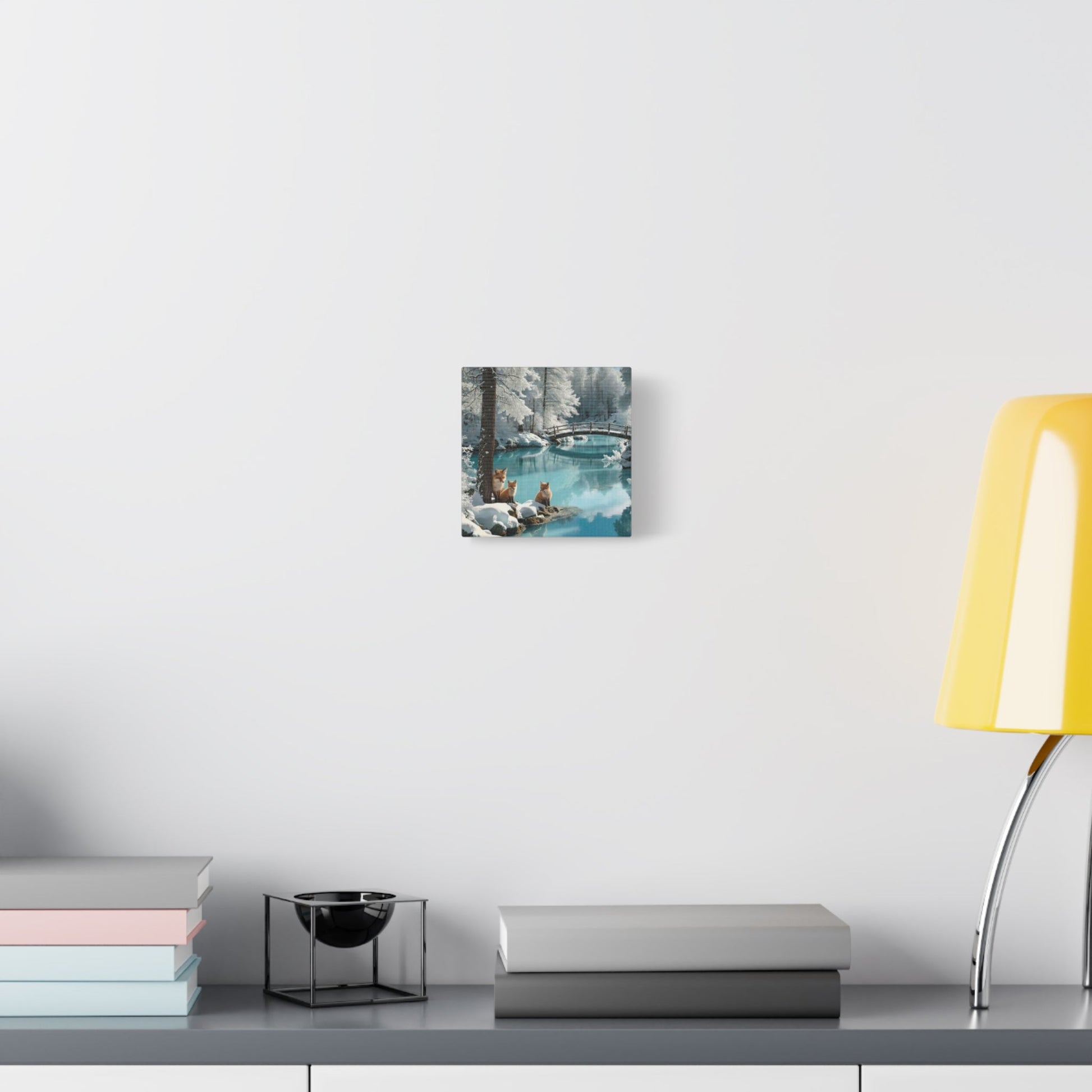Canvas wall art featuring winter landscape with foxes and serene waters on matte finish hanging above a modern desk with books and a yellow lamp